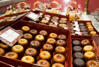 Assortiment de cannelés bordelais et autres pâtisseries fines présentés dans des boîtes rouges avec étiquettes, exposés en vitrine de pâtisserie.
