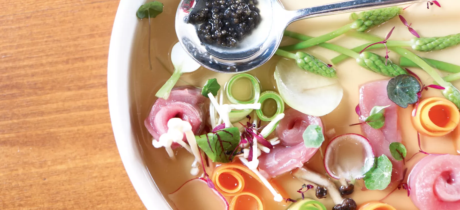 Assiette élégante de fruits de mer et charcuterie bordelaise garnie de caviar, jambon de pays, asperges, olives noires et microgreens, présentée dans un bol blanc sur table en bois.