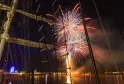 Feu d'artifice multicolore illuminant le ciel nocturne de Bordeaux, vue depuis un voilier avec la Grande Roue et les bâtiments illuminés en arrière-plan