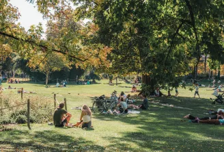 Scène de détente au Jardin public de Bordeaux avec des visiteurs assis sur l'herbe, des arbres aux teintes automnales, et un vélo garé à proximité.