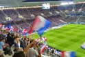 Stade rempli de spectateurs agitant des drapeaux français tricolores lors d'un match de football à Bordeaux, avec les gradins pleins et le terrain visible.