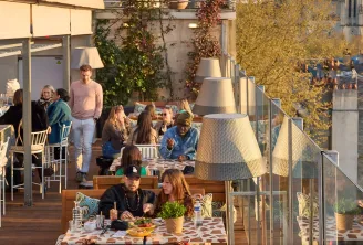 Terrasse rooftop animée à Bordeaux avec clients attablés, vue sur la ville et architecture historique en arrière-plan, décoration végétale et luminaires modernes
